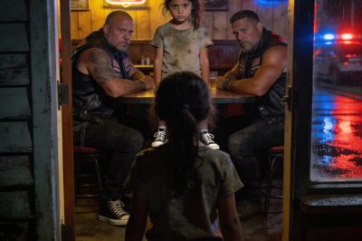 My hands were shaking so hard I could barely open the door. I was seven years old, standing outside the most dangerous biker bar in the county, knowing I had less than ninety seconds to save eight men who terrified everyone in town. I had seen something I wasn’t supposed to see. I saw the man everyone called a “hero”—Sheriff’s Lieutenant David Kaine—kneeling by their motorcycles with plastic bags in his hands. He smiled when he did it. Now, those bikers were inside eating dinner, and the police sirens were already screaming down Route 308. I had to make a choice: stay safe and let innocent men go to prison, or walk into that den of lions and tell the truth. I pushed the door open.